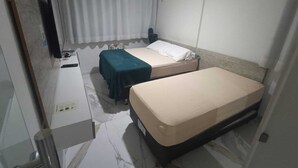 Habitación de hotel con dos camas individuales, un escritorio con silla, televisor de pantalla plana y ventana con cortinas.