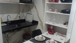 Cocina compacta con microondas, licuadora roja y cafetera. Hay una pequeña mesa de comedor con platos y tazas.