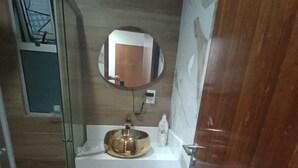Un baño con cabina de ducha de vidrio, un lavabo blanco con recipiente de bronce y suelo de baldosas de mármol.