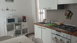 Een kleine keuken met witte kastjes, een magnetron, een gasfornuis en een spoelbak.