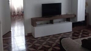 Een woonkamer met een televisie op een houten dressoir, witte muren en een vloer met een patroon.