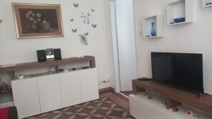 Een moderne woonkamer met een flatscreen televisie, een houten tv-meubel, een witte kast en decoratieve vlinderstickers op de muur.