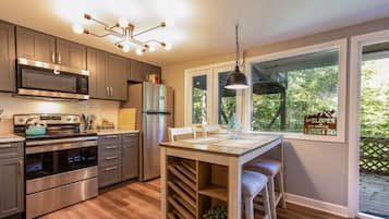 Une cuisine moderne dotée d’appareils électroménagers en acier inoxydable, d’une table à manger en bois et offrant une vue sur l’extérieur grâce à de grandes fenêtres.