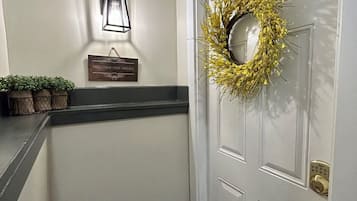 Un couloir avec une porte blanche, une pancarte de bienvenue, un luminaire fixé au mur et une guirlande.