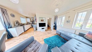 A spacious living room with a sofa, a TV, and a kitchen area in the background. - Sunset Cottage -  a cottage that sleeps 4 guests  in 2 bedrooms (Filey)