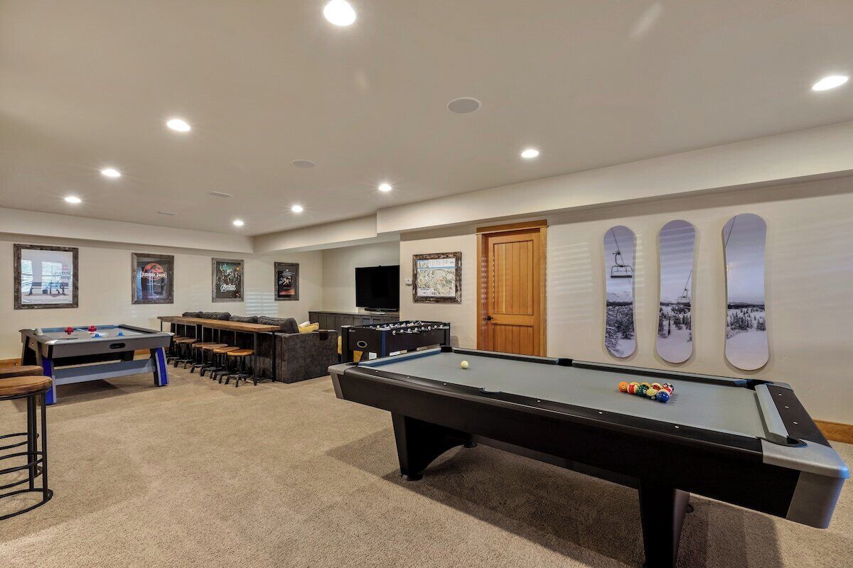 A pool table, foosball table, and bar area in a room with a ski-themed wall.
