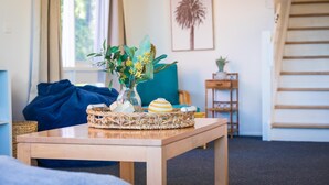 A wooden table with a woven basket, a vase with flowers, and a striped object. - Tathra Beach Shack - Pet Friendly (Tathra)