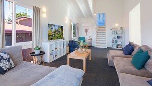 A modern living room with a sofa, a coffee table, and a bookshelf. - Tathra Beach Shack - Pet Friendly (Tathra)
