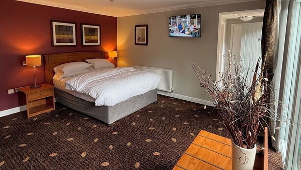 A hotel room with a bed, a bedside table, a TV, and a window with curtains.