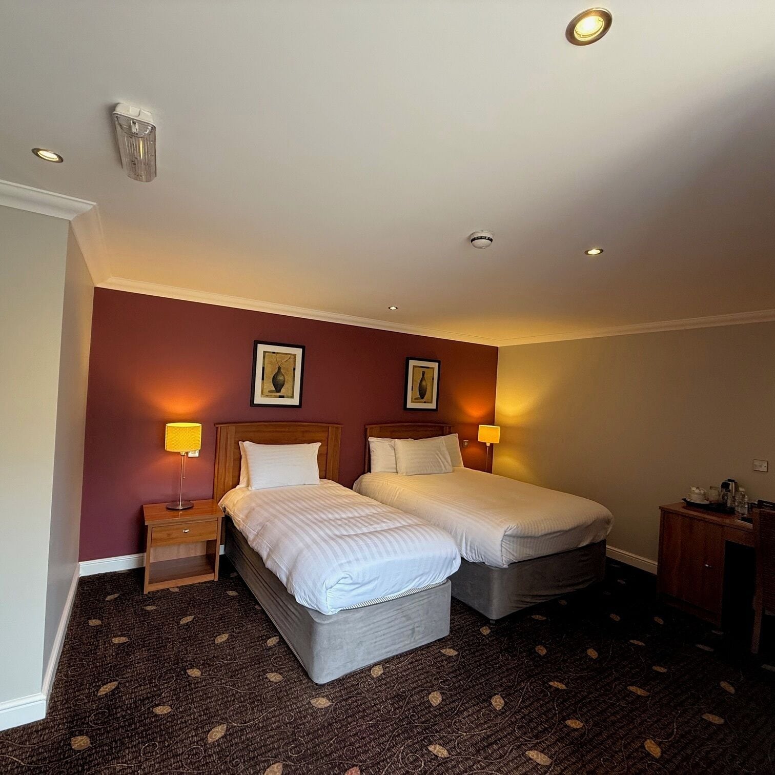 A hotel room with two beds, a wooden nightstand, a desk, and a chair.