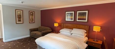 A hotel room with a bed, two bedside lamps, a chair, and two framed pictures on the wall.