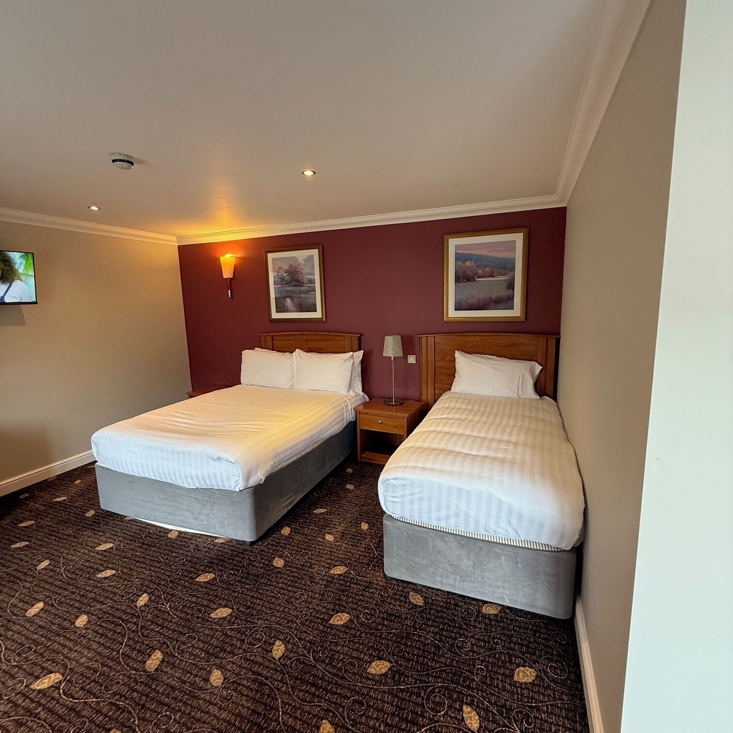 Une chambre d’hôtel avec deux lits, une télévision et deux lampes fixées au mur.