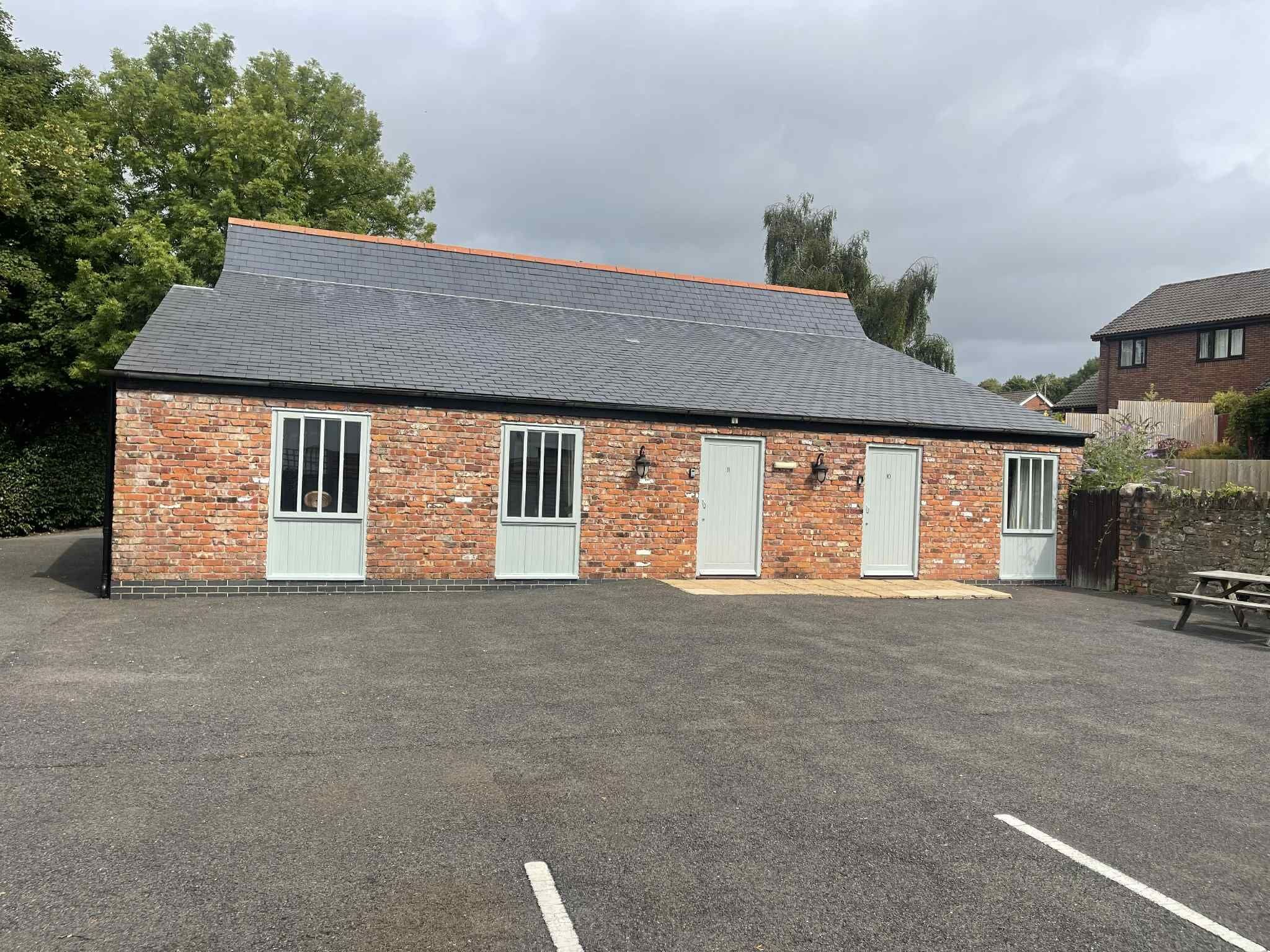 A brick building with a sloped roof, three doors, and windows.