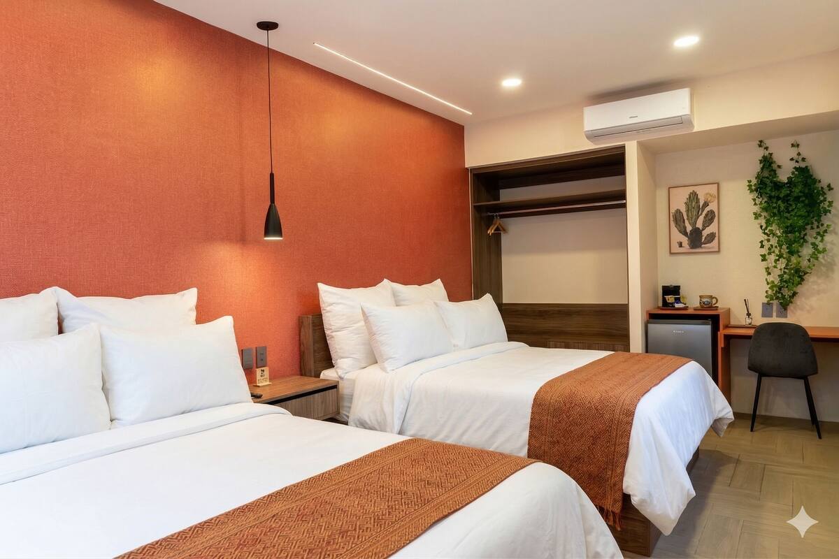 A hotel room with two beds, a desk, a chair, an air conditioner, and a plant.