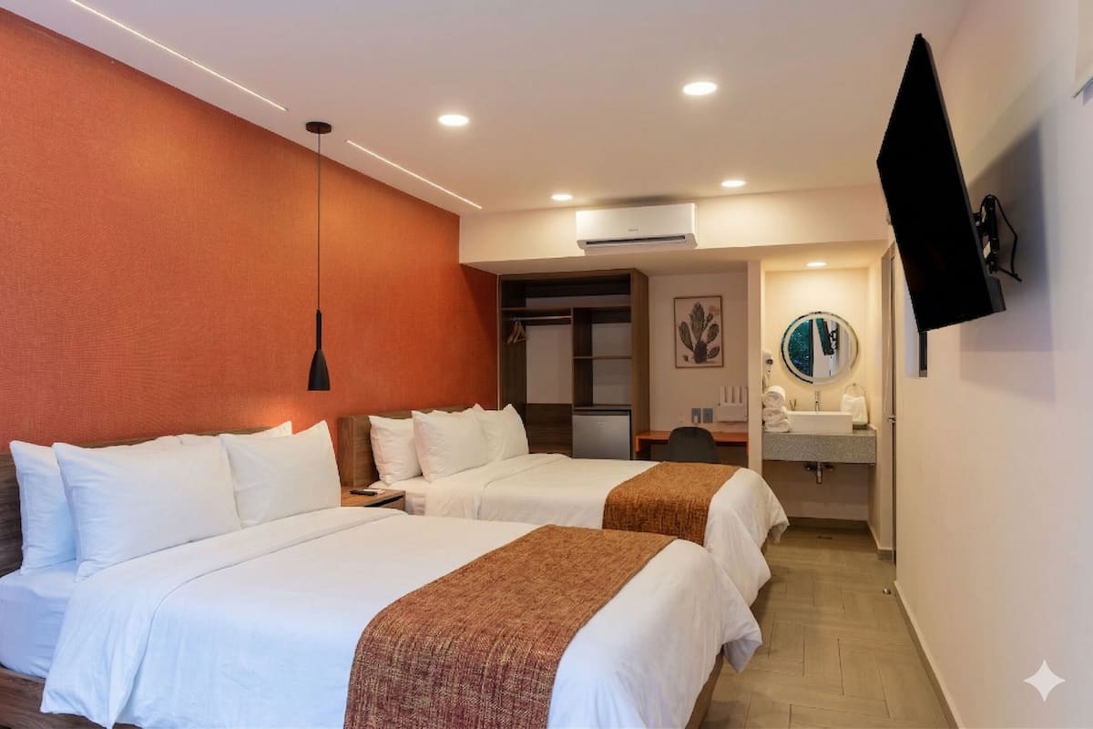 A hotel room with two beds, a TV, a desk, a mirror, and a bathroom.