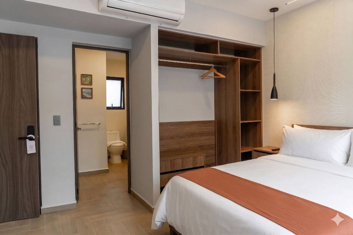 A hotel room with a bed, a wardrobe, a bedside table, and a hanging light fixture.