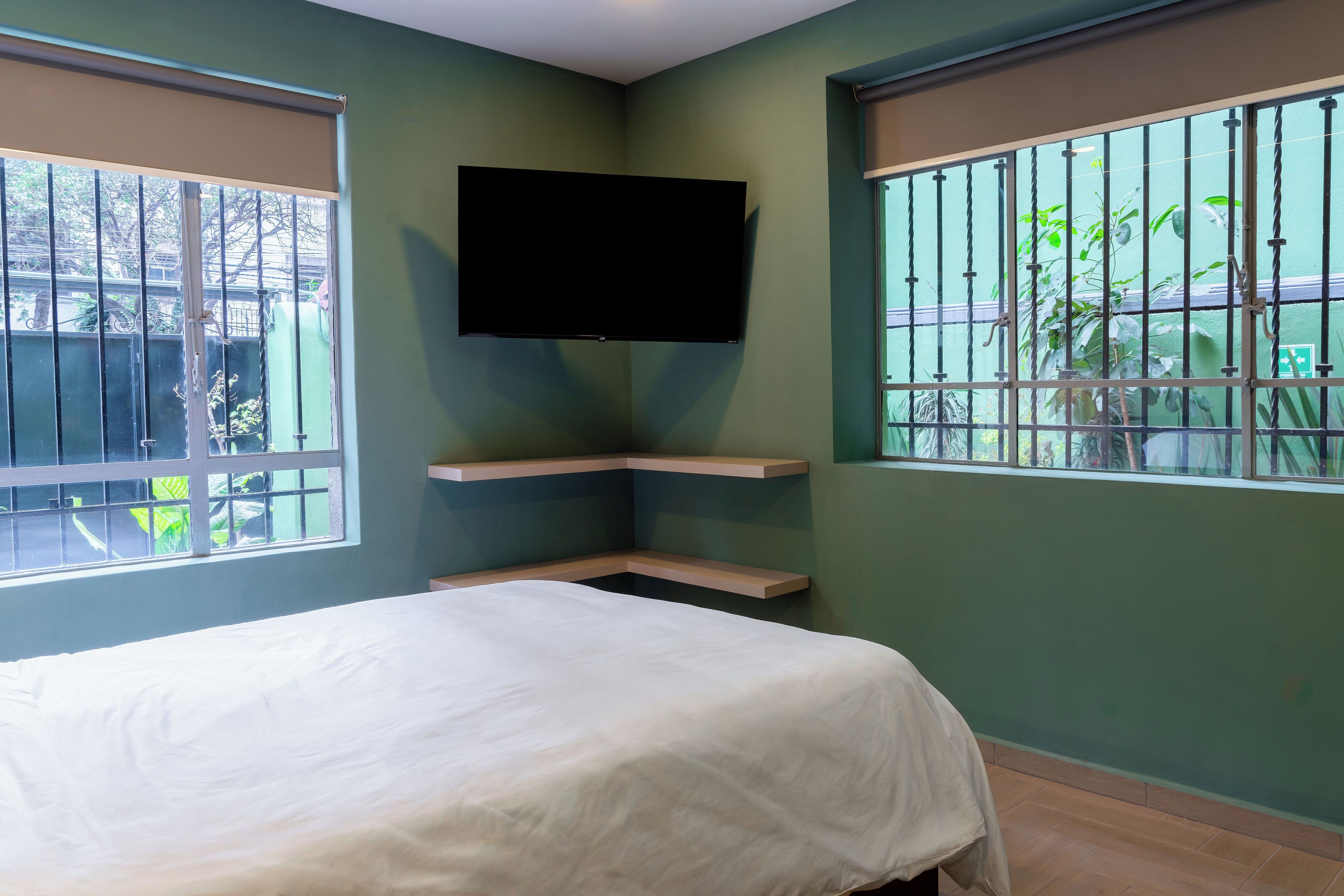 Una habitación con cama, televisor montado y ventanas con rejas.