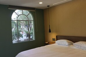 A bedroom with a large arched window, a bed with white linens, a bedside table, and a hanging pendant light. - Atrio Polanco (Mexico City)