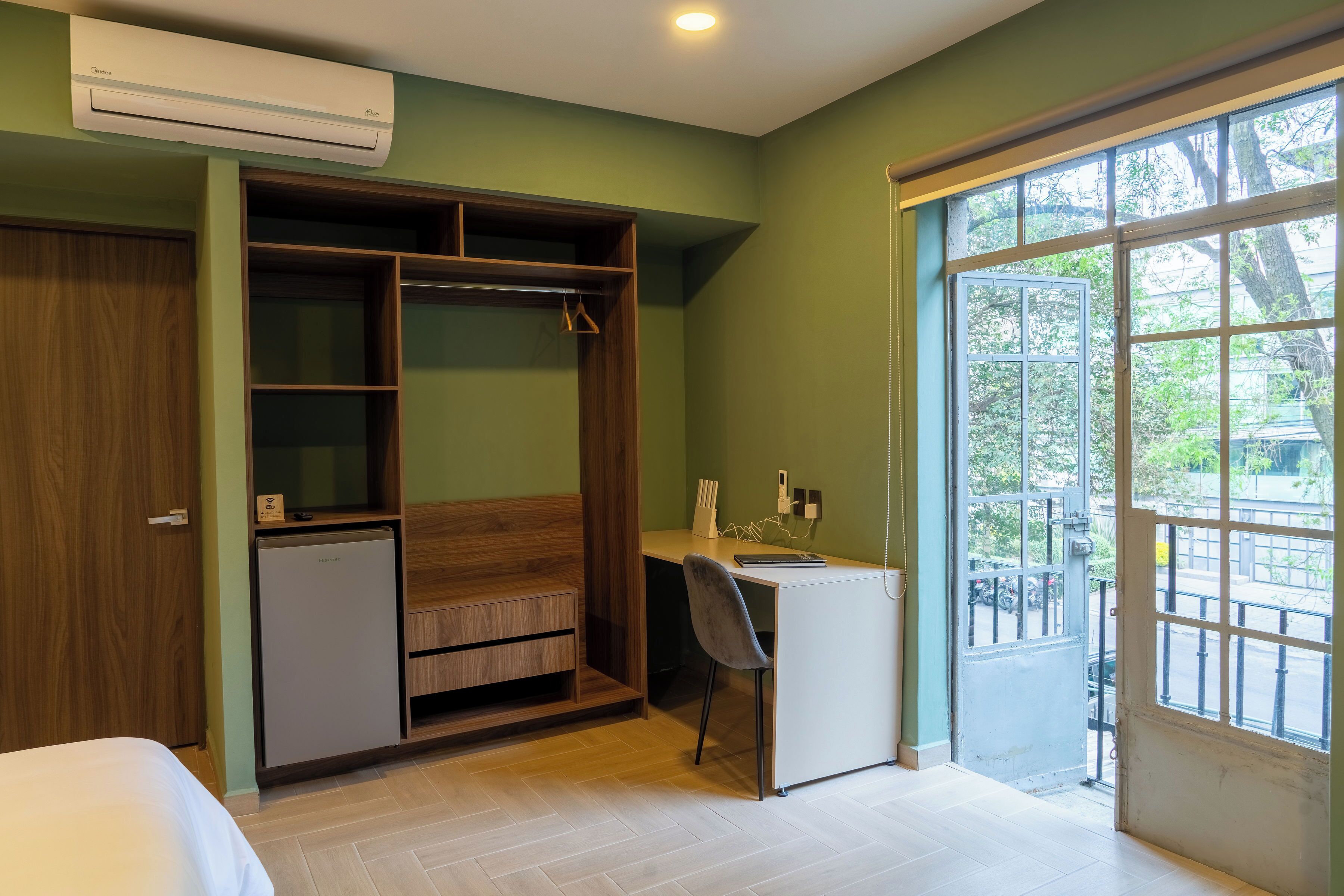 A room with a bed, a desk, a wardrobe, and a balcony with a view.