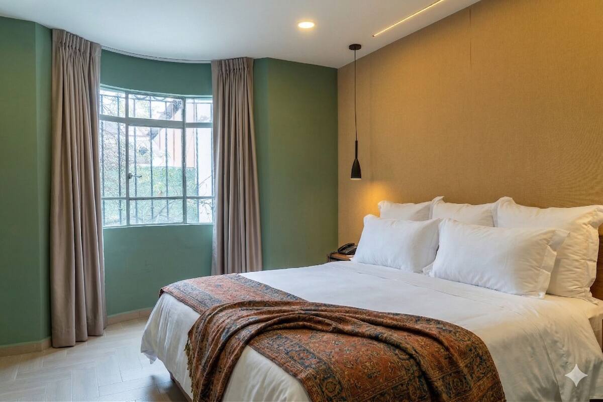 A bedroom with a large bed, a nightstand, a lamp, and a window with curtains.