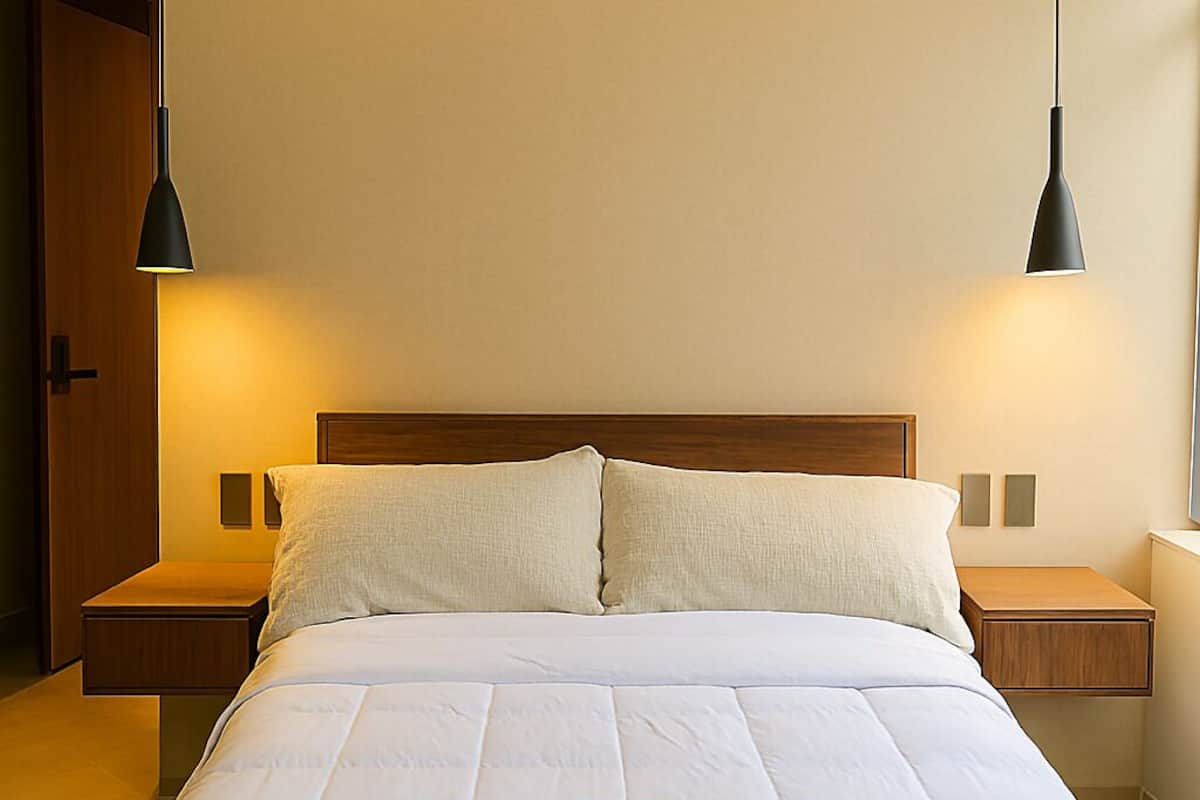 A neatly made bed with a wooden headboard, two bedside tables, and two wall-mounted lamps.