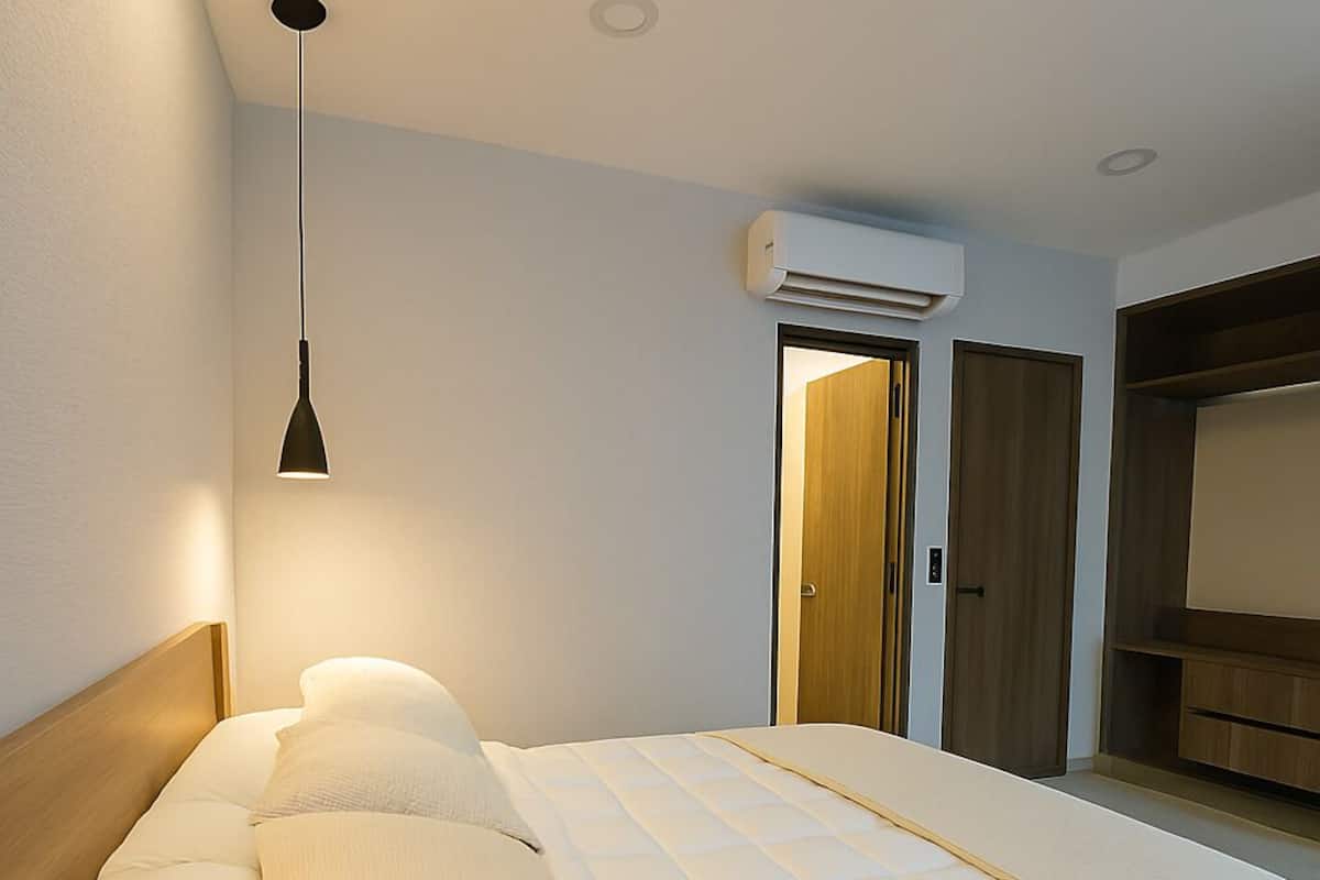 A modern bedroom with a bed, bedside tables, a hanging light, an air conditioning unit, and a wardrobe.