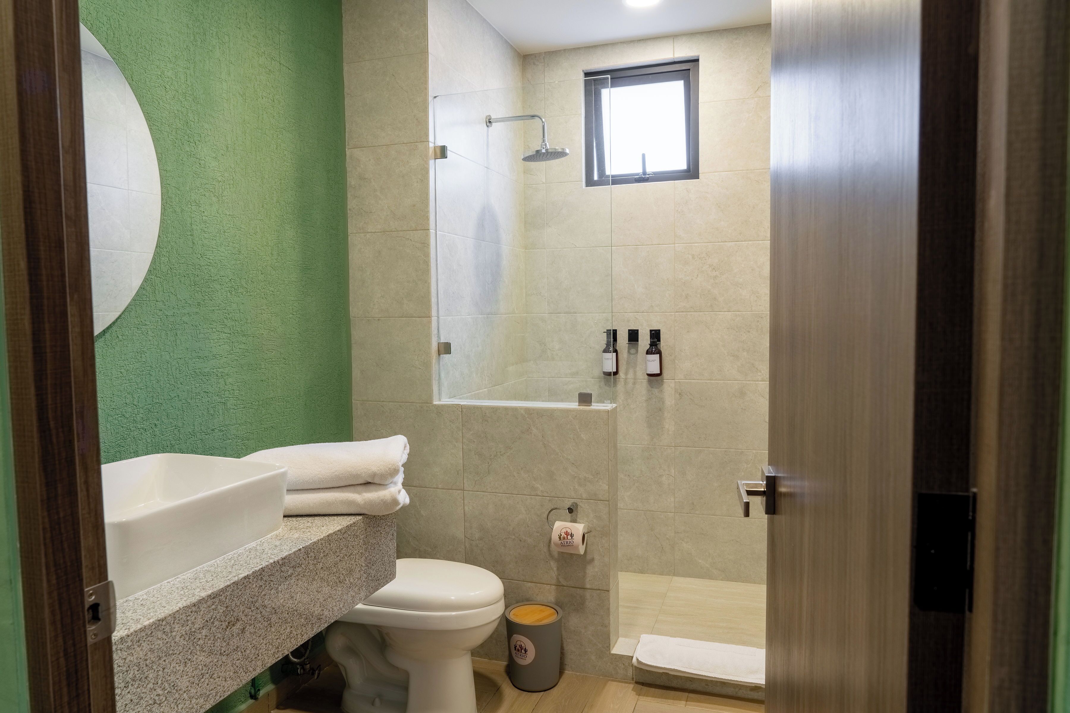 A bathroom with a toilet, sink, shower, and a small window.