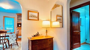 Een kamer met een houten dressoir, een spiegel en een lamp. Er is een eethoek met een tafel en stoelen zichtbaar op de achtergrond.