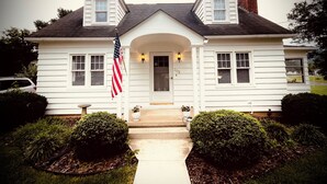Een wit huis met twee verdiepingen, een centrale ingang, een schoorsteen en een Amerikaanse vlag.
