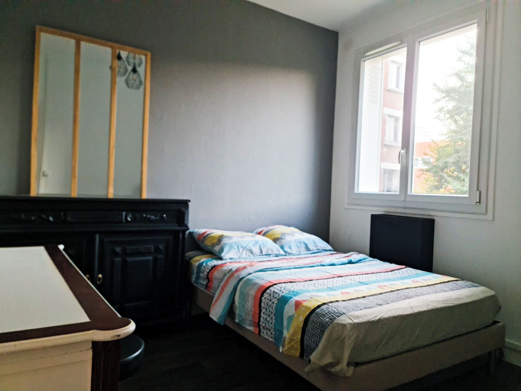A bedroom with a bed, a dresser, a window, and a mirror.