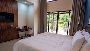 Une chambre d’hôtel dotée d’un grand lit, d’un bureau avec un ordinateur portable, d’un téléviseur fixé au mur et d’un balcon avec une chaise et un fauteuil suspendu.