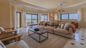 A spacious living room with a large sofa, a coffee table, and a view of the outdoors through large windows. - 184 - Ocean Views Golf Villa (Cascais)