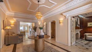 A spacious lobby with a round wooden table, a sofa, and a floor lamp. There are decorative vases and a potted plant on the table. - 184 - Ocean Views Golf Villa (Cascais)