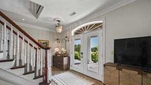 Un vestíbulo amplio con una escalera de madera, un candelabro, un televisor grande y vistas al exterior.