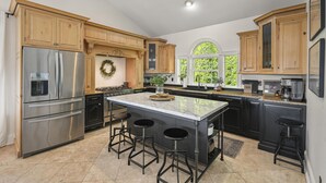 Una cocina moderna con armarios de madera, electrodomésticos de acero inoxidable, una isla grande con taburetes y vistas a zonas verdes a través de las ventanas.