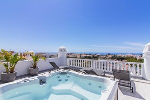 Eine Dachterrasse mit Whirlpool, Liegestühlen und Topfpflanzen.