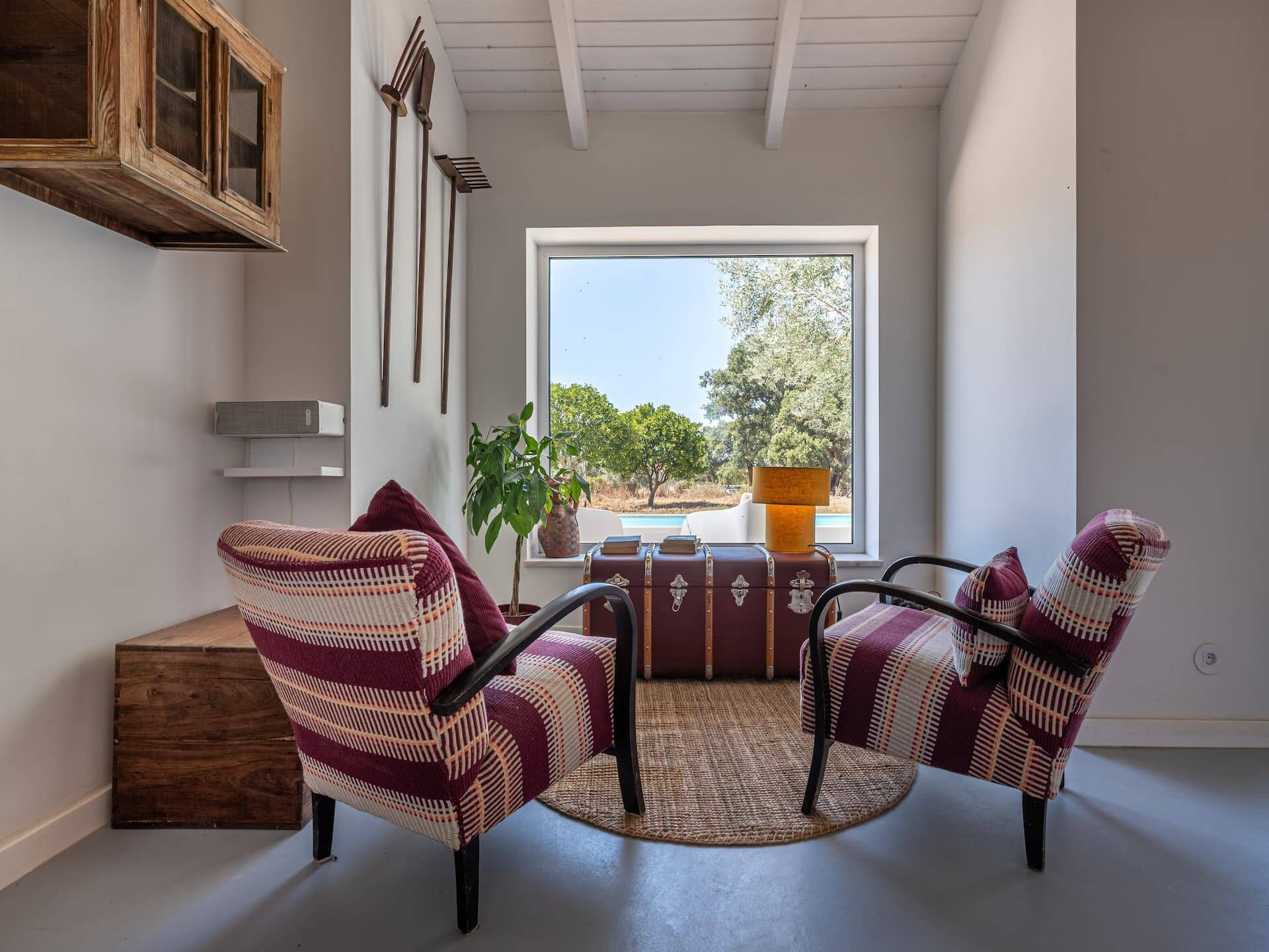 A cozy seating area with two patterned armchairs, a small table, and a view of trees through a window.