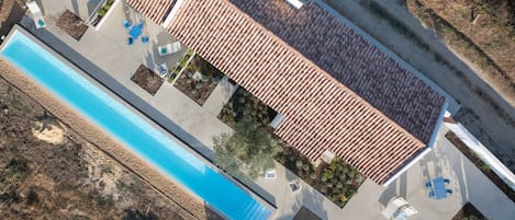 An aerial view of a property with a swimming pool, outdoor seating, and a tiled roof.