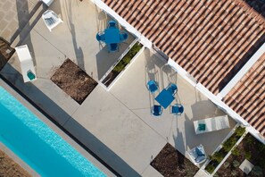 An aerial view of a rooftop terrace with a swimming pool, blue outdoor furniture, and a tiled roof.