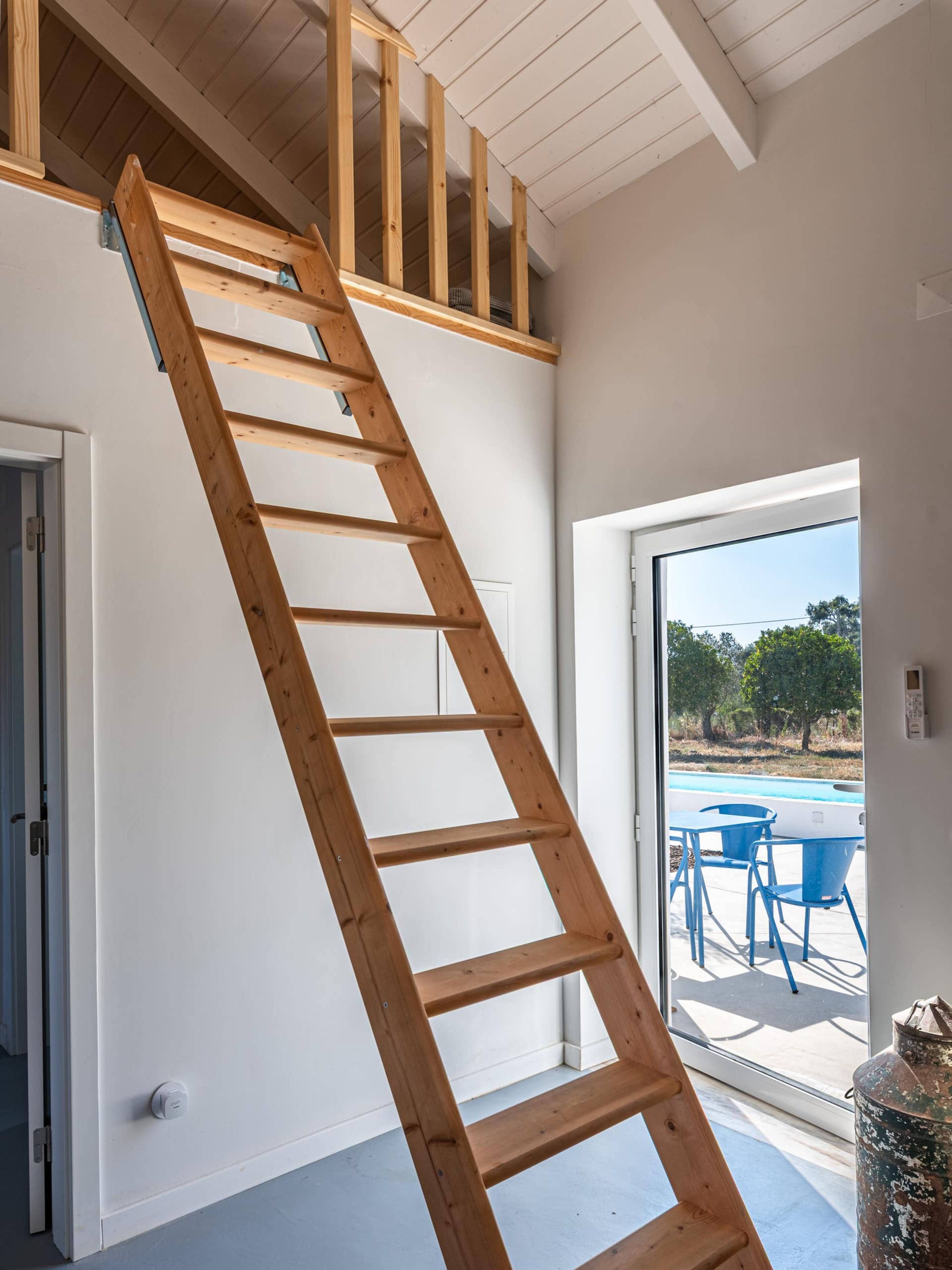 A wooden interior staircase leading to an upper floor, with a view of an outdoor swimming pool through a glass door.