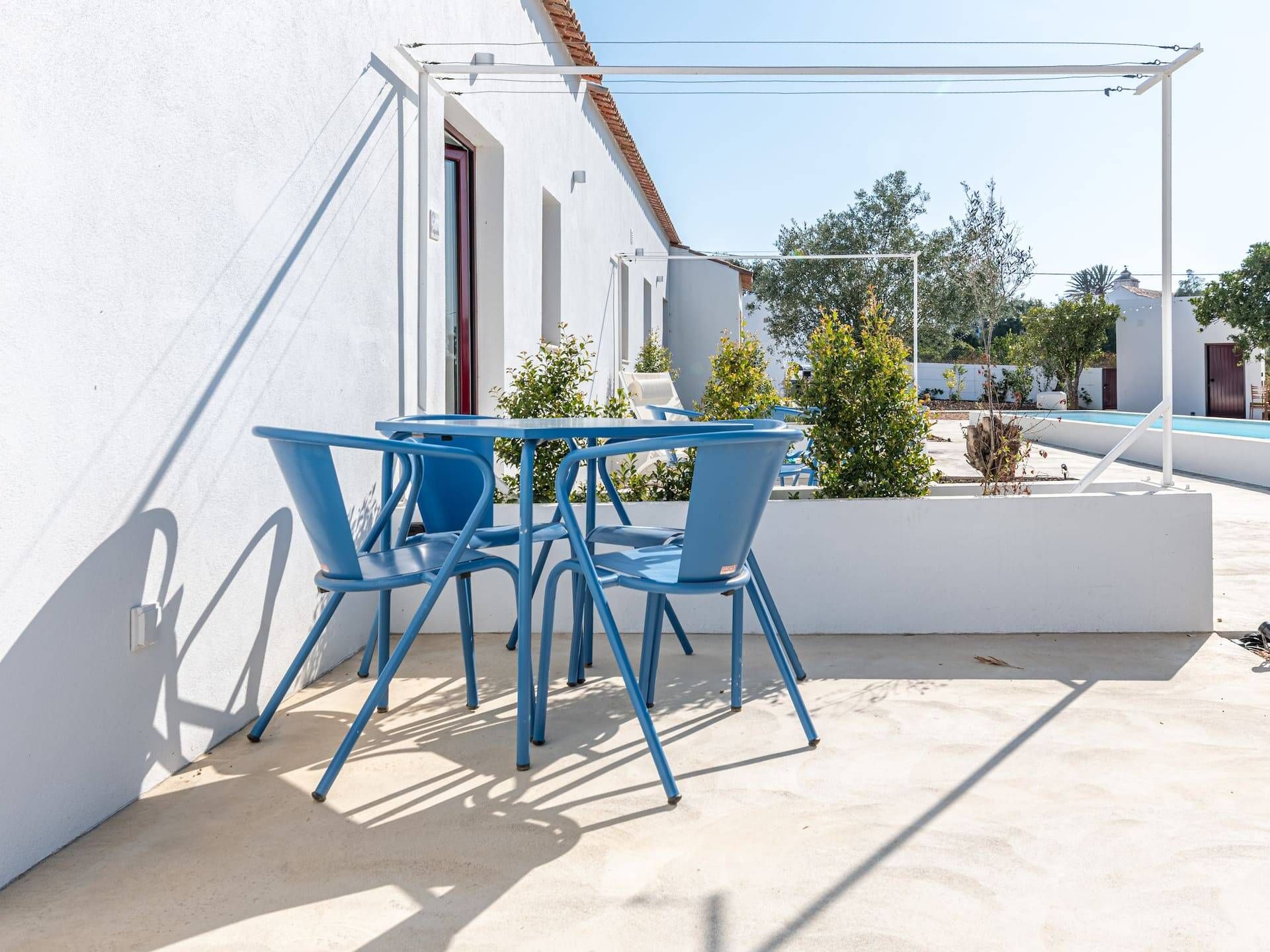Un patio con una mesa y sillas, una piscina y un edificio blanco con puerta roja.