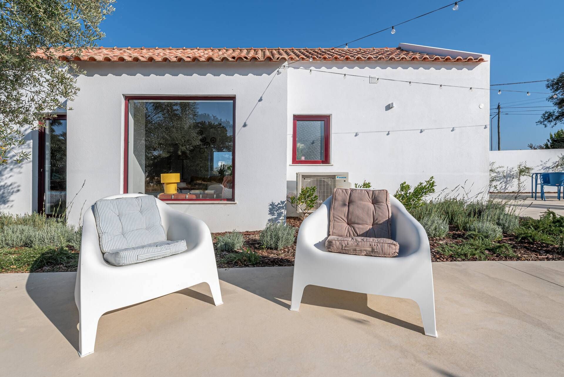 Una casa moderna con fachada blanca, techo de tejas y dos sillas blancas en el exterior.