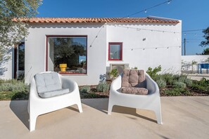A modern house with a white exterior, a tiled roof, and two white chairs outside.