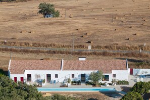 A white building with a tiled roof, a swimming pool, and outdoor seating.