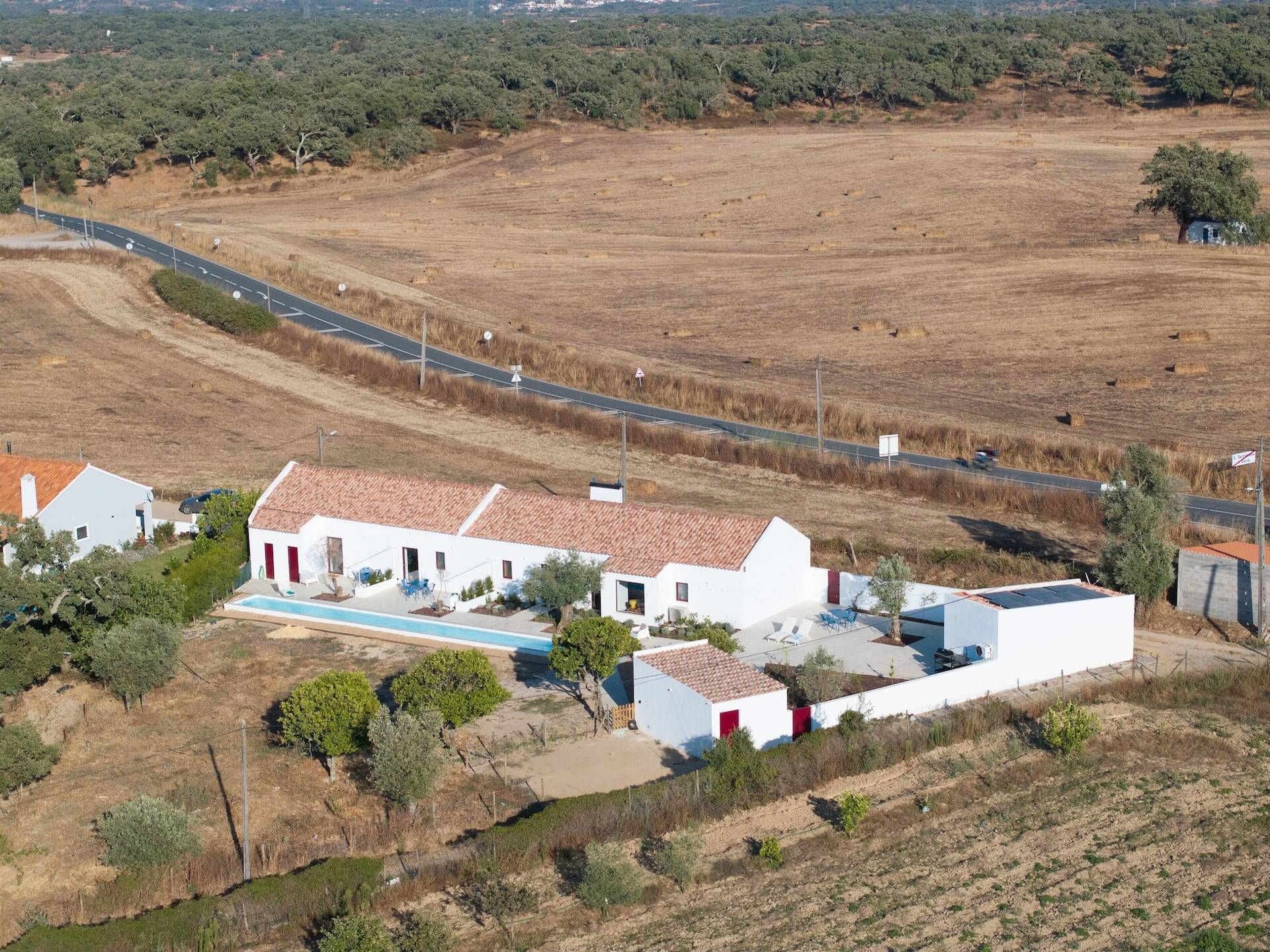 Um edifício branco com telhado vermelho, piscina e quintal cercado.
