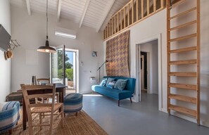 Een ruime woonkamer met een blauwe bank, een houten trap en een eethoek.