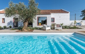 Une maison moderne avec une piscine, deux chaises blanches et un arbre.