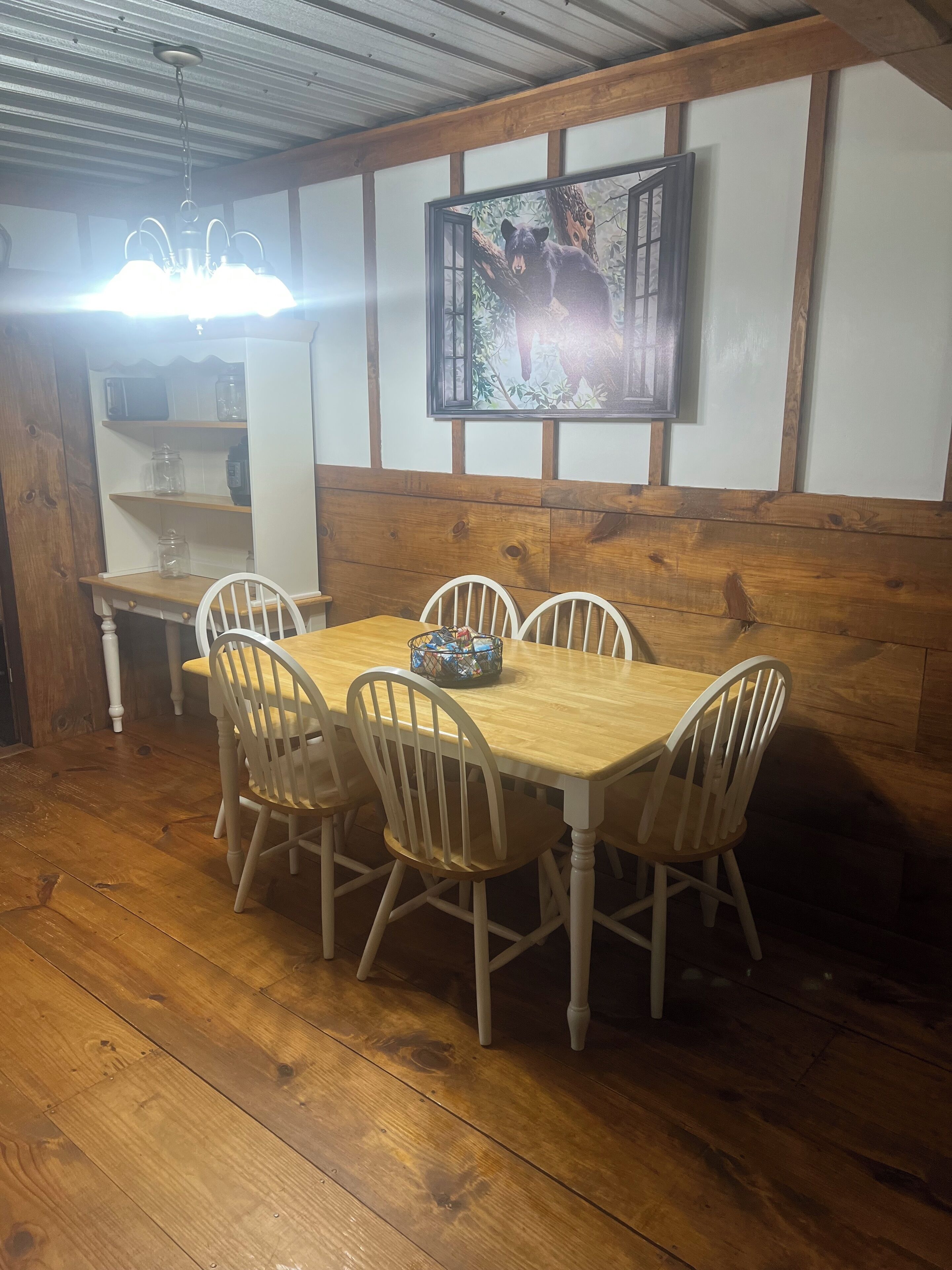 Un comedor con una mesa y sillas de madera, una araña y un cuadro en la pared.
