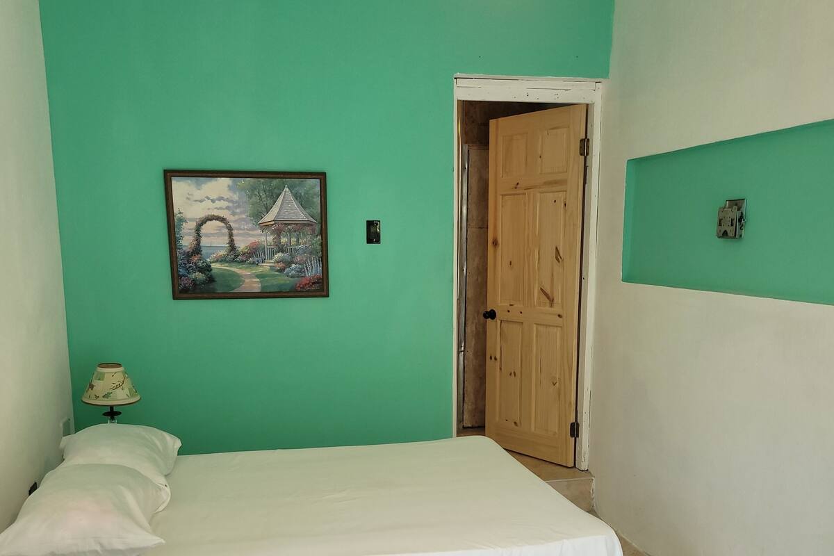 Una habitación con una cama, una puerta, un cuadro y una lámpara.
