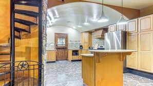A spacious kitchen with a central island, a stone-tiled floor, and wooden cabinetry. - Italian-Styled Home w/ Lake Views & Private Pool (Belton)